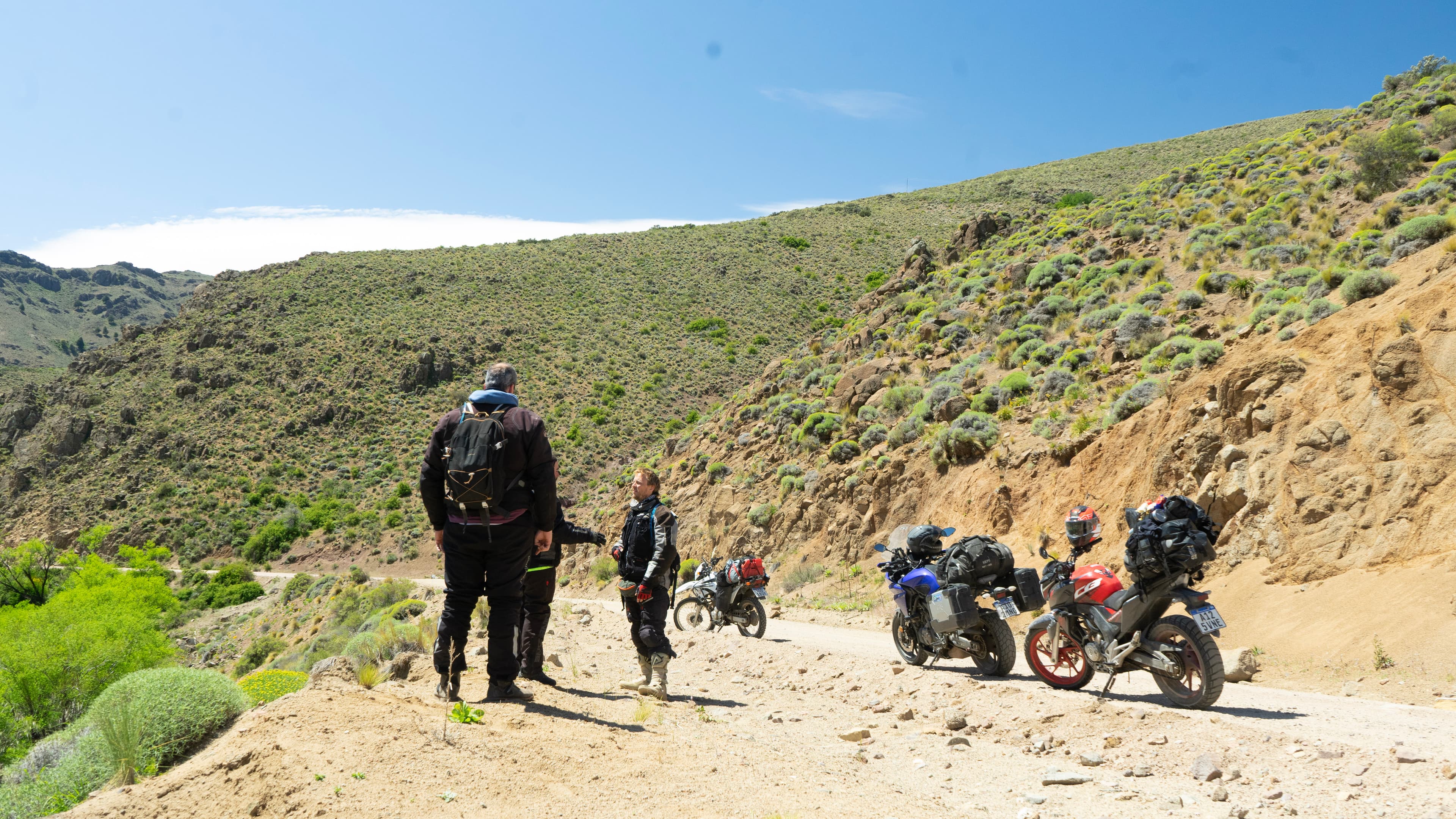 Pilotos junto a motos cargadas en un camino de ripio durante Cruces del Sur.