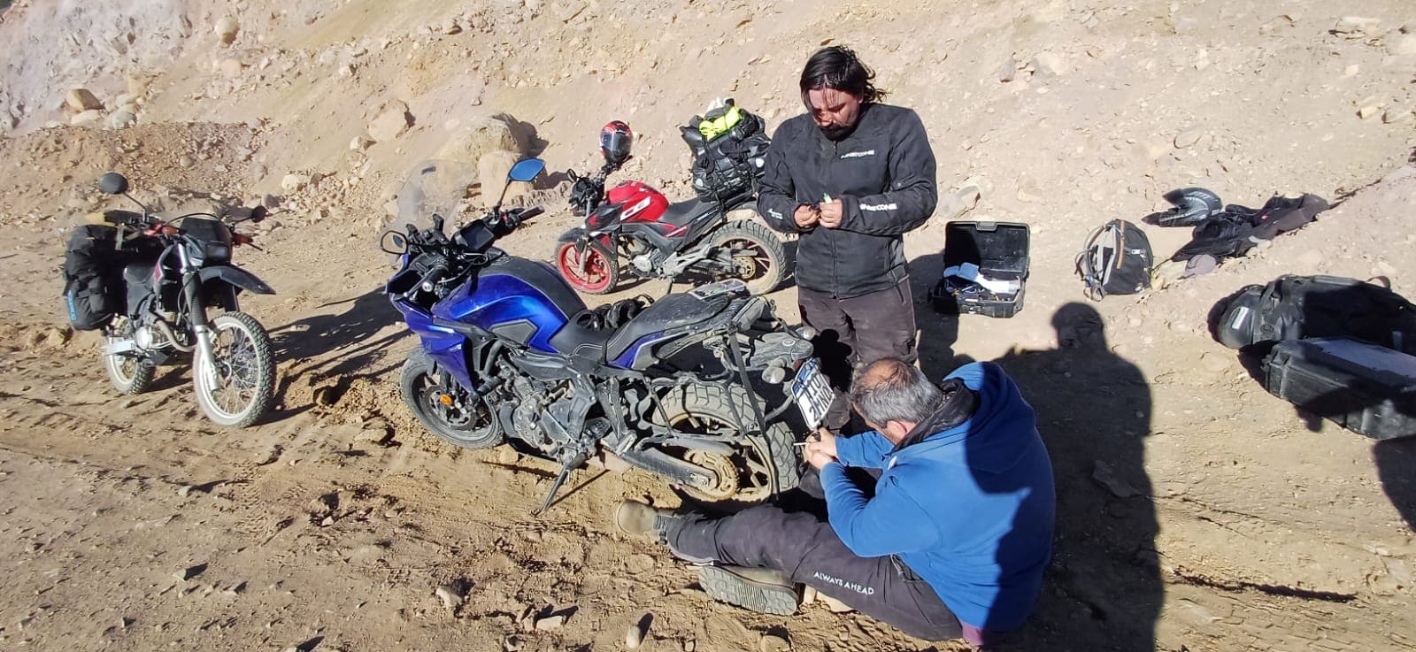 Equipo reparando una moto en una ladera seca durante una exploración de Salta y Jujuy.